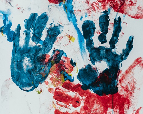 A pair of blue fingerpainted hands on a paint-covered wall.